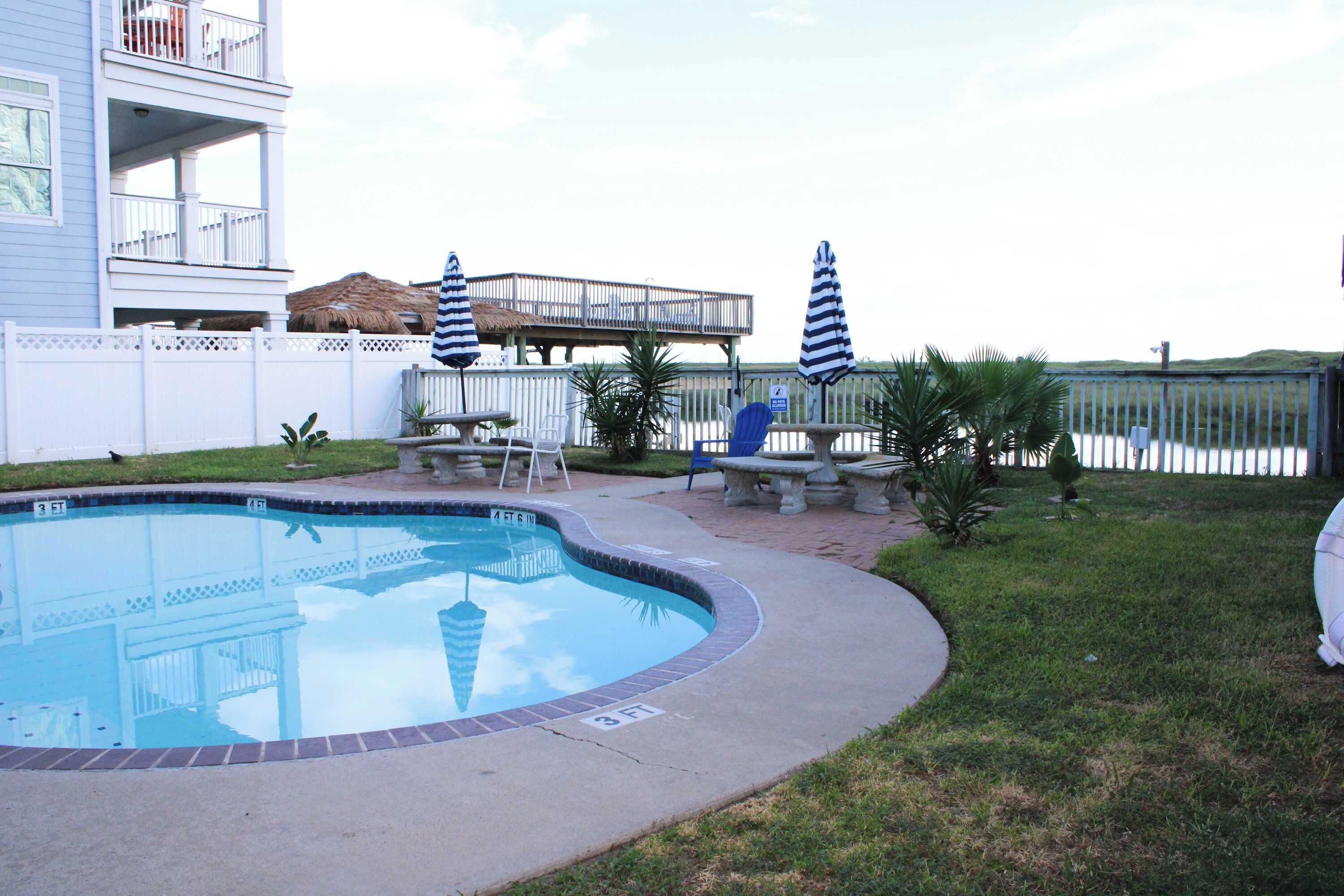 Una piscina con una terraza alrededor, un área de descanso cubierta y vistas a un edificio con balcones.
