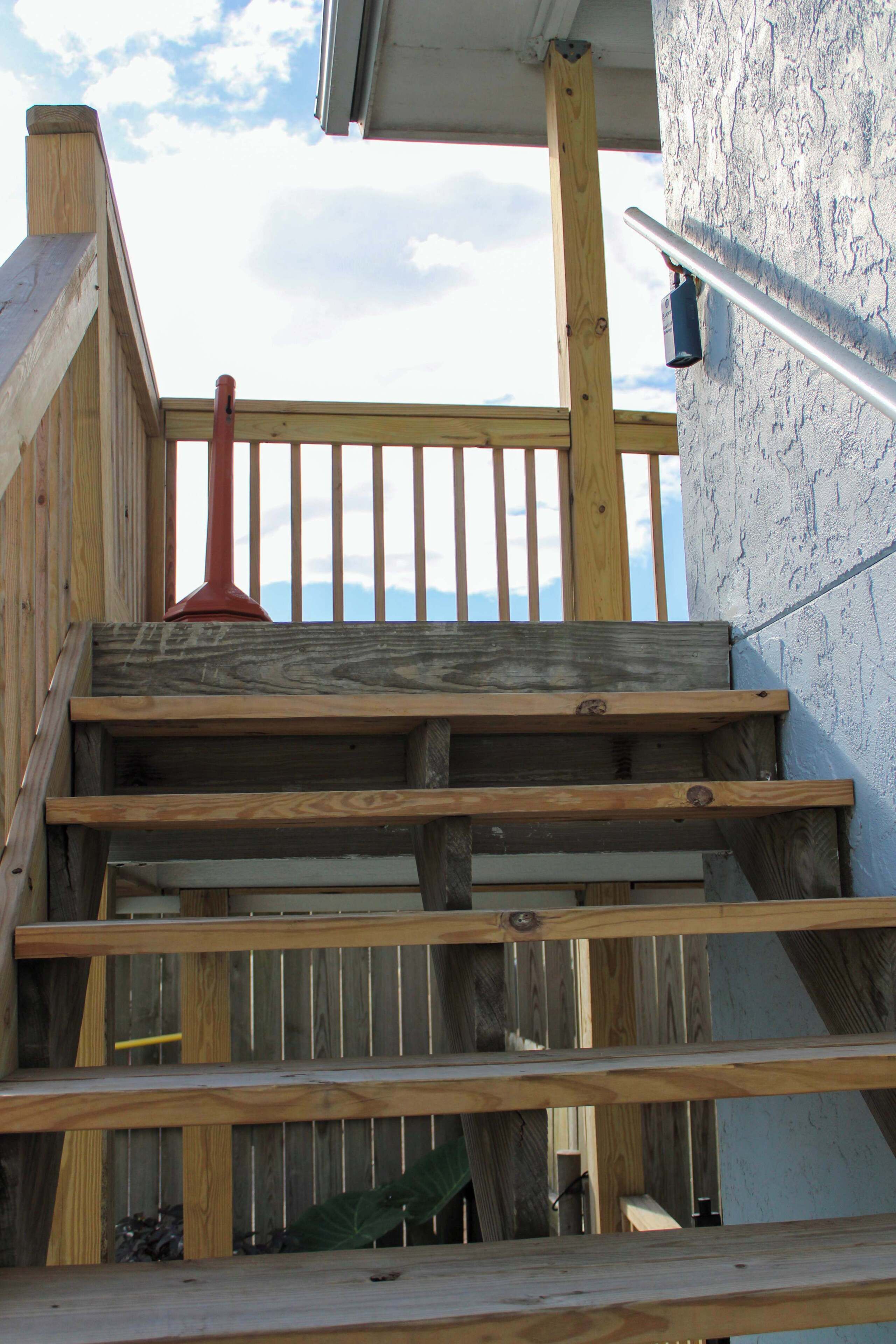 Eine Holztreppe führt zu einem Balkon mit Geländer und einem Metallhandlauf, mit Blick auf den Himmel.
