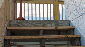 Eine Holztreppe führt zu einem Balkon mit Geländer und einem Metallhandlauf, mit Blick auf den Himmel.