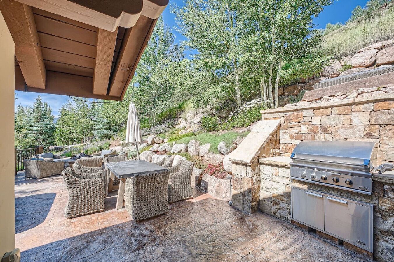 Une terrasse extérieure avec des meubles en osier, un barbecue en pierre et un muret de soutènement en pierre.