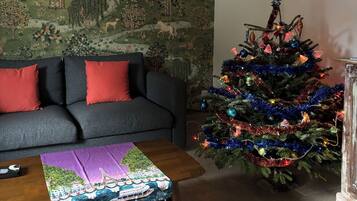 Ein Wohnzimmer mit einer Couch, einem Couchtisch mit Tischdecke, einem Weihnachtsbaum und einer Wand mit einem Wandgemälde zum Thema Natur.