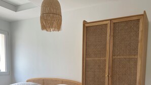 Ein Schlafzimmer mit einem Bett, einem Rattanschrank und einer Pendelleuchte.