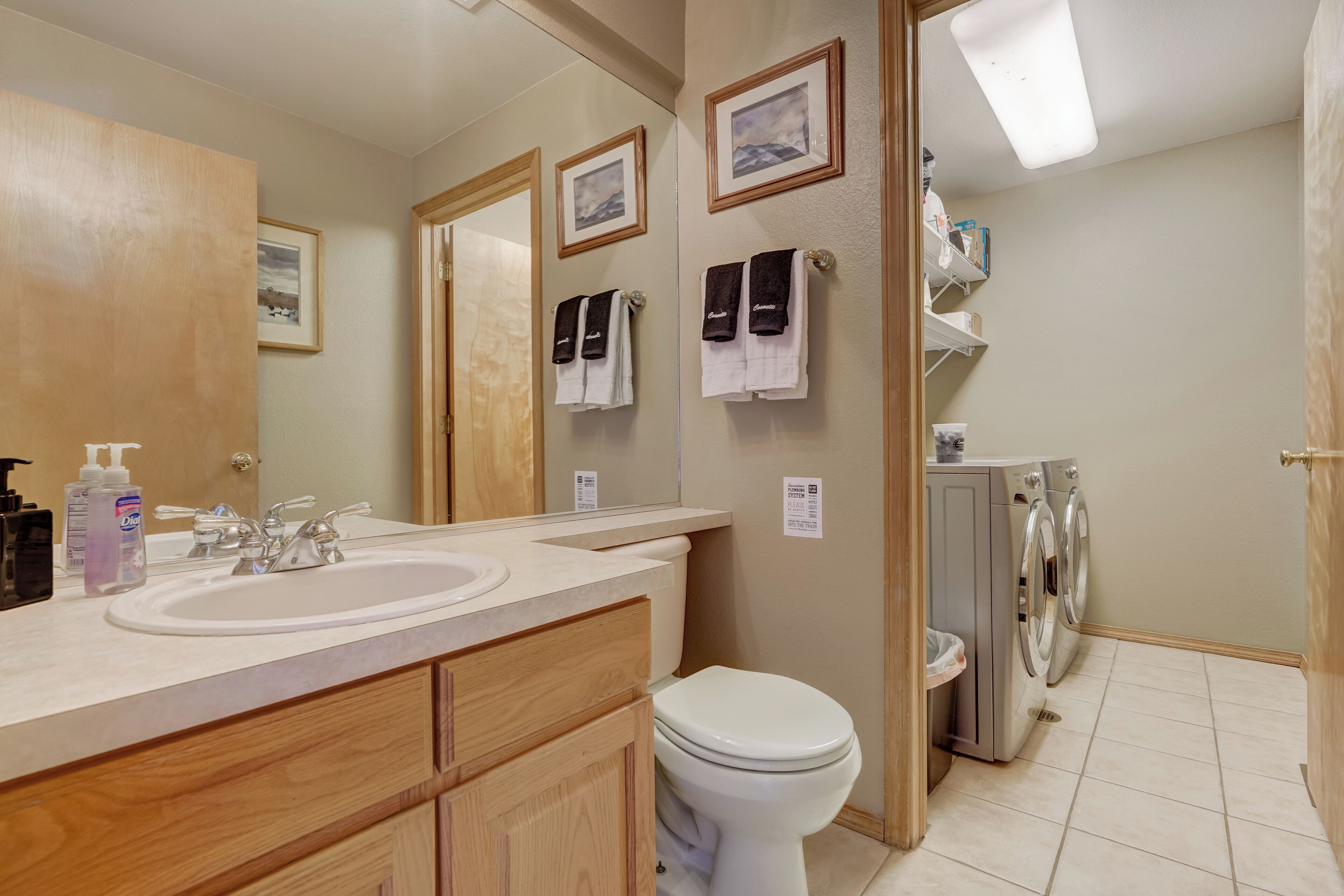 Een moderne badkamer met een dubbele wastafel, houten kastjes, een toilet en een ingebouwde wasmachine.