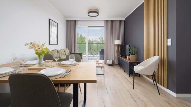 Ein moderner Essbereich mit Holztisch, gedeckt für zwei Personen, einer Couch und einem Fernseher auf einem Schrank.