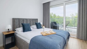 Ein modernes Hotelzimmer mit einem großen Bett, einem Nachttisch, einem kleinen Tisch mit Frühstücksgebäck und einem Balkon mit Stuhl.