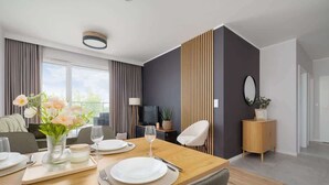 Ein stilvoller Essbereich mit einem Holztisch, gedeckt für vier Personen, einer Blumenvase und einem Fernseher im Hintergrund.