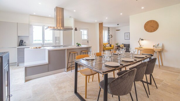 A modern kitchen with a central island, a dining area with a wooden table and chairs, and a living space with a sofa and a clock on the wall. - 10 minutes from the prestigious Av de Champagne in EPERNAY, Maison à la Campagne. (Athis)