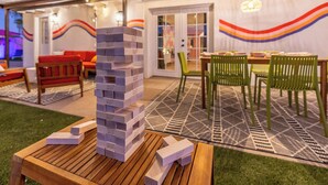 Un espace de détente extérieur accueillant, avec une table en bois, une pile de blocs de jeu Jenga et une fresque murale colorée.
