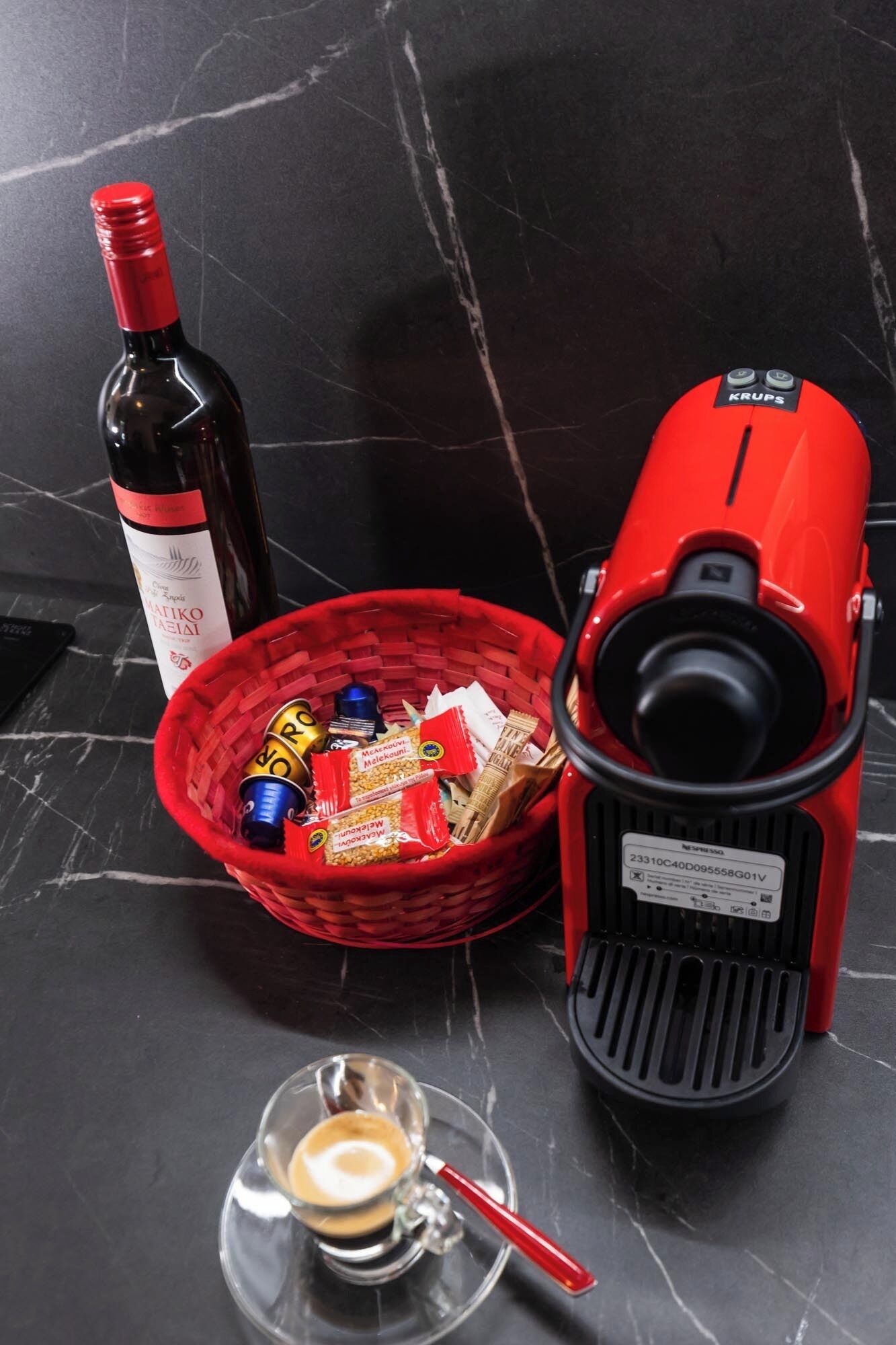 Eine Weinflasche, ein roter Korb mit Snacks, eine Kaffeemaschine und eine Tasse Kaffee auf einer Marmorplatte.