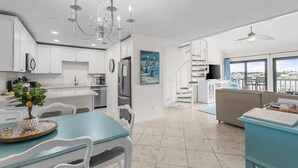 A modern kitchen with white cabinetry, a dining area with a blue table, a staircase, and a living area with a view. - Waterfront Condo Nearby Beach Boat Slip sleeps 12! (Orange Beach)