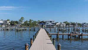A pier leading to a waterfront property with a dock, a covered area, and houses in the background. - Waterfront Condo Nearby Beach Boat Slip sleeps 12! (Orange Beach)