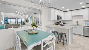 A modern kitchen with white cabinetry, a central island, stainless steel appliances, and a teal dining table with white chairs. - Waterfront Condo Nearby Beach Boat Slip sleeps 12! (Orange Beach)