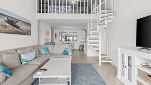 A modern living room with a sofa, coffee table, and a TV. There's a staircase leading to a loft area with a bed. - Waterfront Condo Nearby Beach Boat Slip sleeps 12! (Orange Beach)