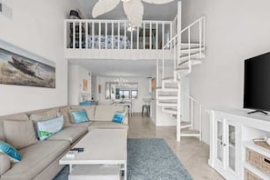 A modern living room with a high ceiling, a staircase, a sofa, a coffee table, and a television. - Waterfront Condo Nearby Beach Boat Slip sleeps 12! (Orange Beach)