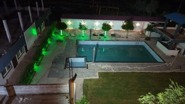 Una piscina con un piccolo solarium, circondata da un portico coperto con sedute e alberi.