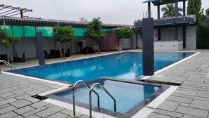 Una piscina rettangolare all'aperto con bordo piastrellato, circondata da un muretto basso e un'area relax coperta.