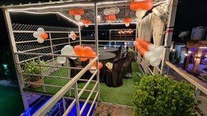 Un'area salotto all'aperto con tavoli e sedie, circondata da un recinto metallico e decorata con palloncini.