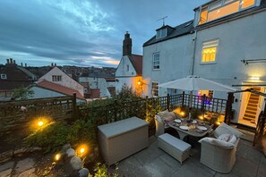 A patio area with outdoor furniture, a table set for dining, and a view of the surrounding neighborhood.