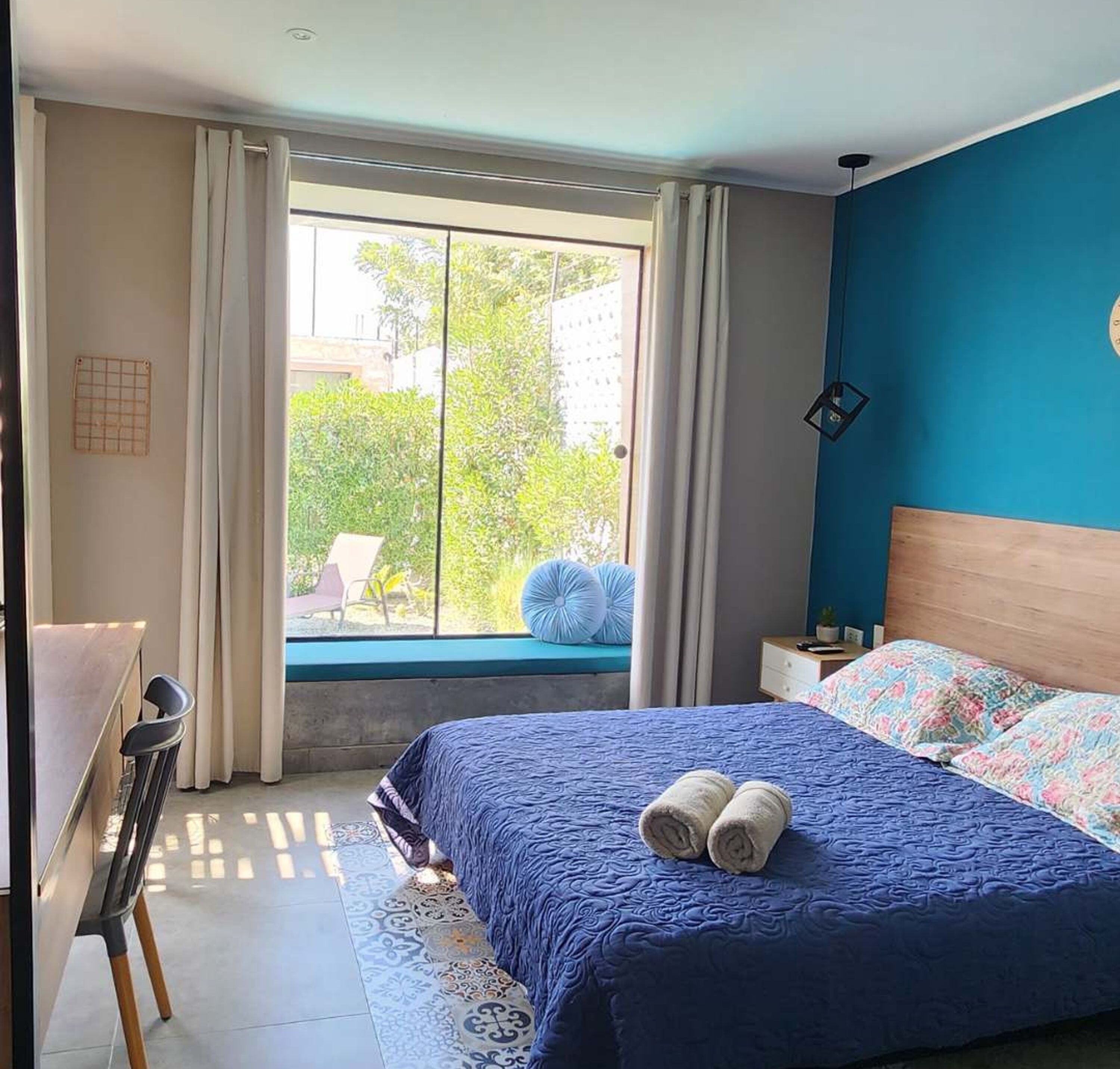 A bedroom with a large bed, a desk, and a view of greenery outside.