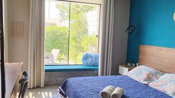 A bedroom with a large bed, a desk, and a view of greenery outside.