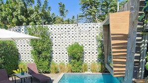 Zwembad met een terras met een geometrisch patroon, omringd door diverse planten en een houten hek.
