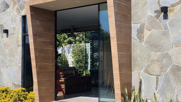 Een modern gebouw met een stenen gevel, een glazen ingang en een klein terras.