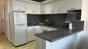 Een moderne keuken met witte kasten, een granieten werkblad, een ingebouwde magnetron en een roestvrijstalen koelkast.