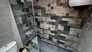 Een badkamer met douche, toilet en een betegelde muur.