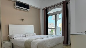 Ein ordentlich bezogenes Bett mit weißen Laken, ein Nachttisch und eine Wand-Klimaanlage.