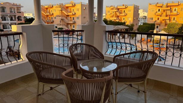 Ein Balkon mit Korbstühlen und Blick auf einen Swimmingpool und Gebäude.