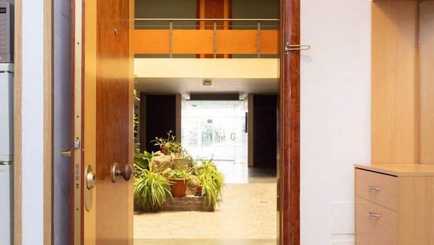 Puerta abierta que da a un espacio amplio con balcón, un armario de madera y suelo de baldosas.