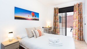 Habitación de hotel con cama, escritorio, silla, mesita de noche y un cuadro de globos aerostáticos.
