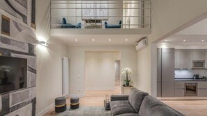 Una sala moderna con un sofá gris, una alfombra pequeña y una escalera que lleva a un balcón con sillas azules.