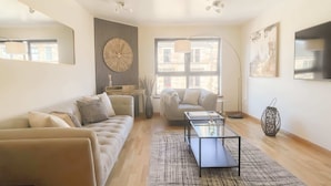 A modern living room with a sofa, a coffee table, and a TV. There is a large window providing natural light and a view of the outside. - Great George Lane Sum (Glasgow City)