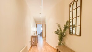 A hallway with a wooden bench, a radiator, a plant, and a window with a decorative frame. - Great George Lane Sum (Glasgow City)