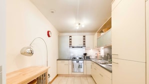 A compact kitchen with a stove, oven, and sink, a wooden table, and a red clock on the wall. - Great George Lane Sum (Glasgow City)