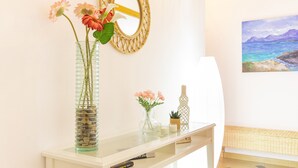 A white console table with a glass vase containing flowers, a small potted plant, and a decorative bottle.