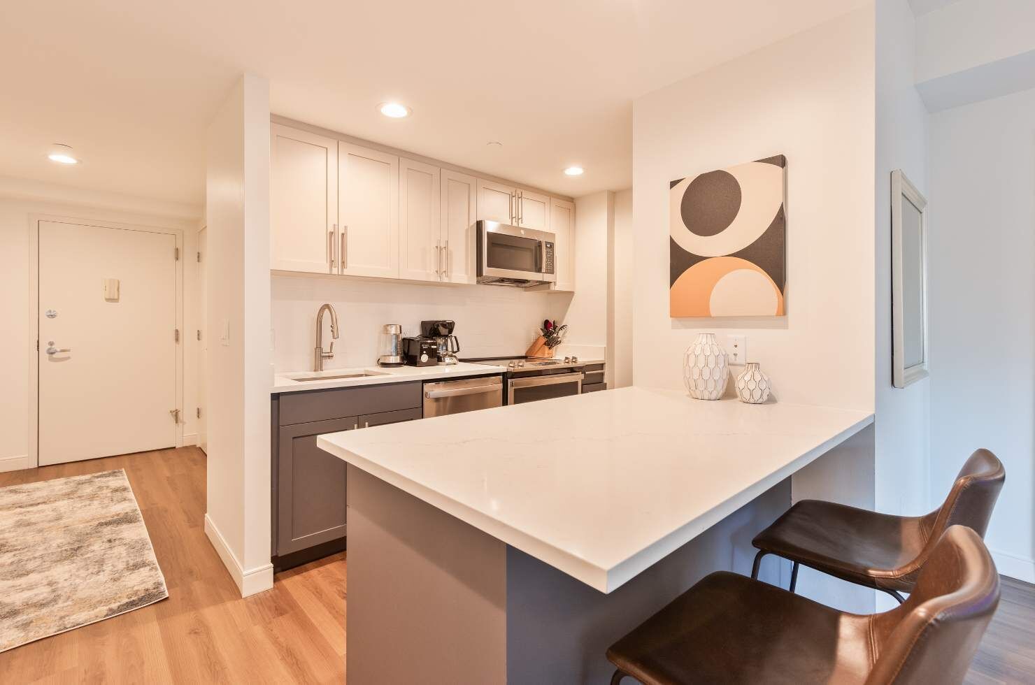 A modern kitchen with white cabinets, a microwave, and a coffee maker. There are two bar stools and a large island.