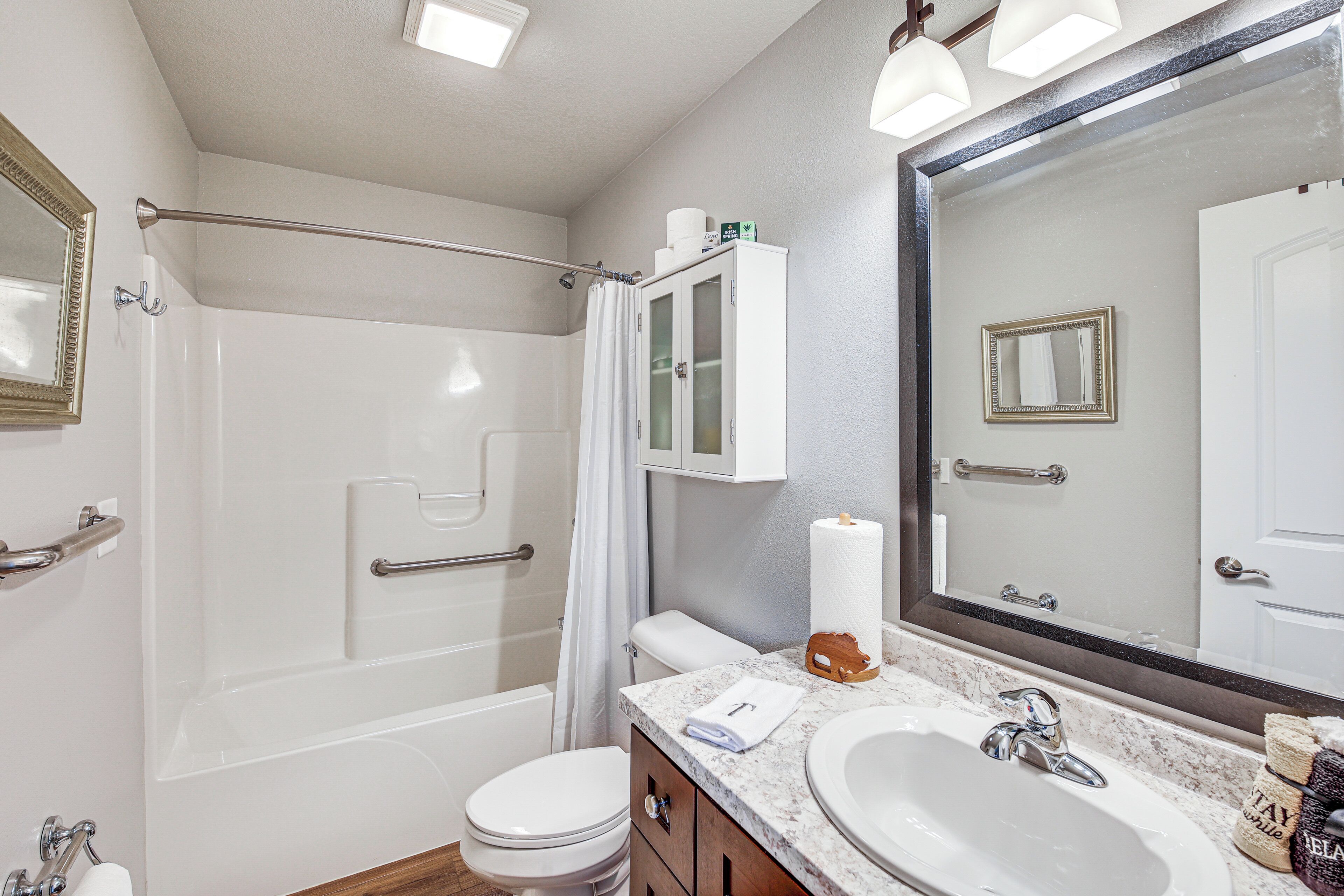 A bathroom with a shower, toilet, vanity with a sink, and a large mirror.