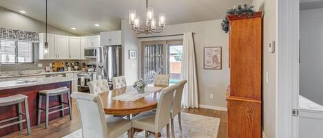 A spacious kitchen with white cabinets, a wooden dining table with six chairs, and a chandelier.