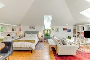 A spacious loft bedroom with a large bed, a seating area with a sofa and armchair, a glass coffee table, and a TV.