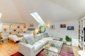 Een moderne loft slaapkamer met dakraam, een witte bank, een glazen salontafel en een boekenkast.