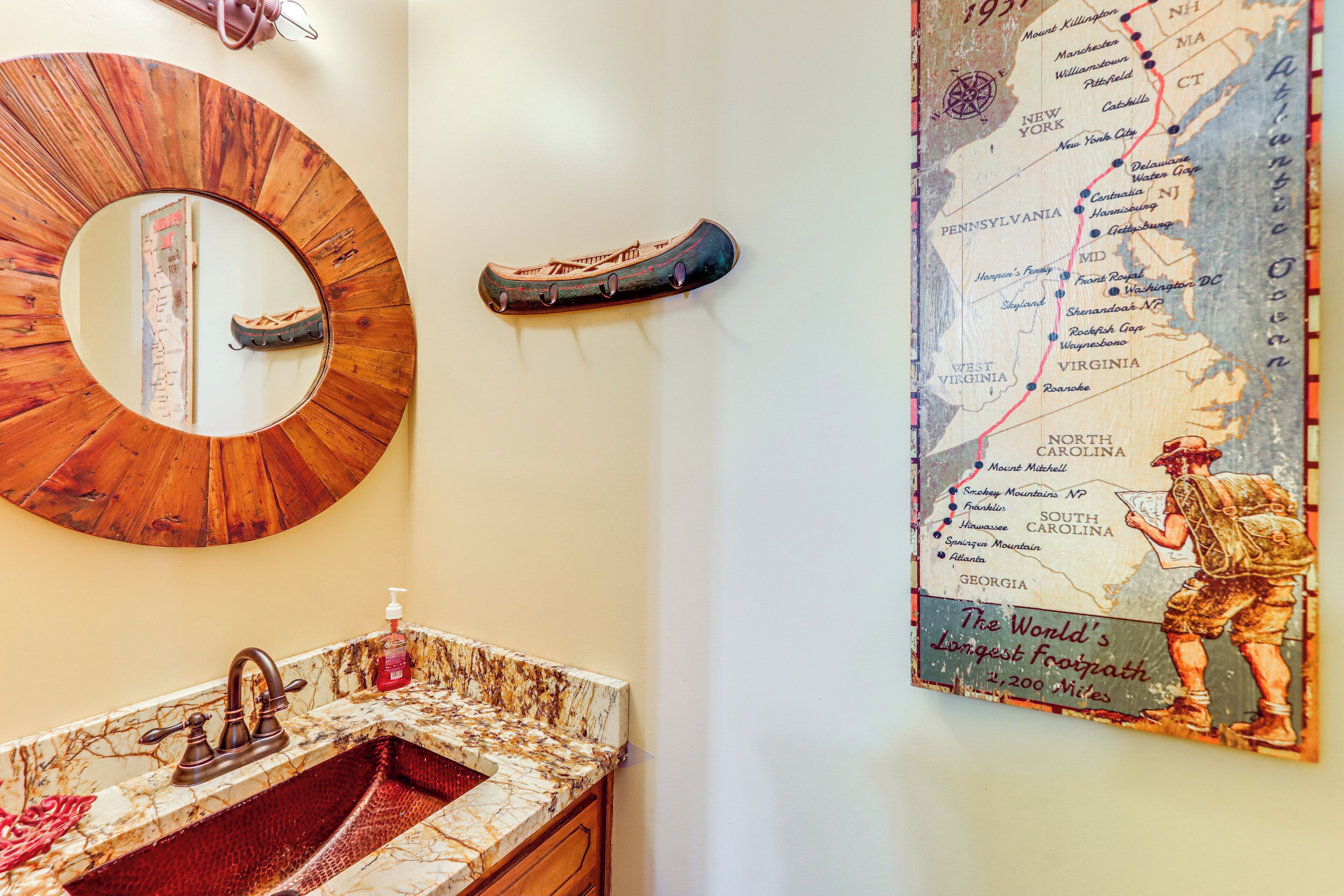 A bathroom with a round mirror, a sink with a marble countertop, and a map of the world's longest footpath.