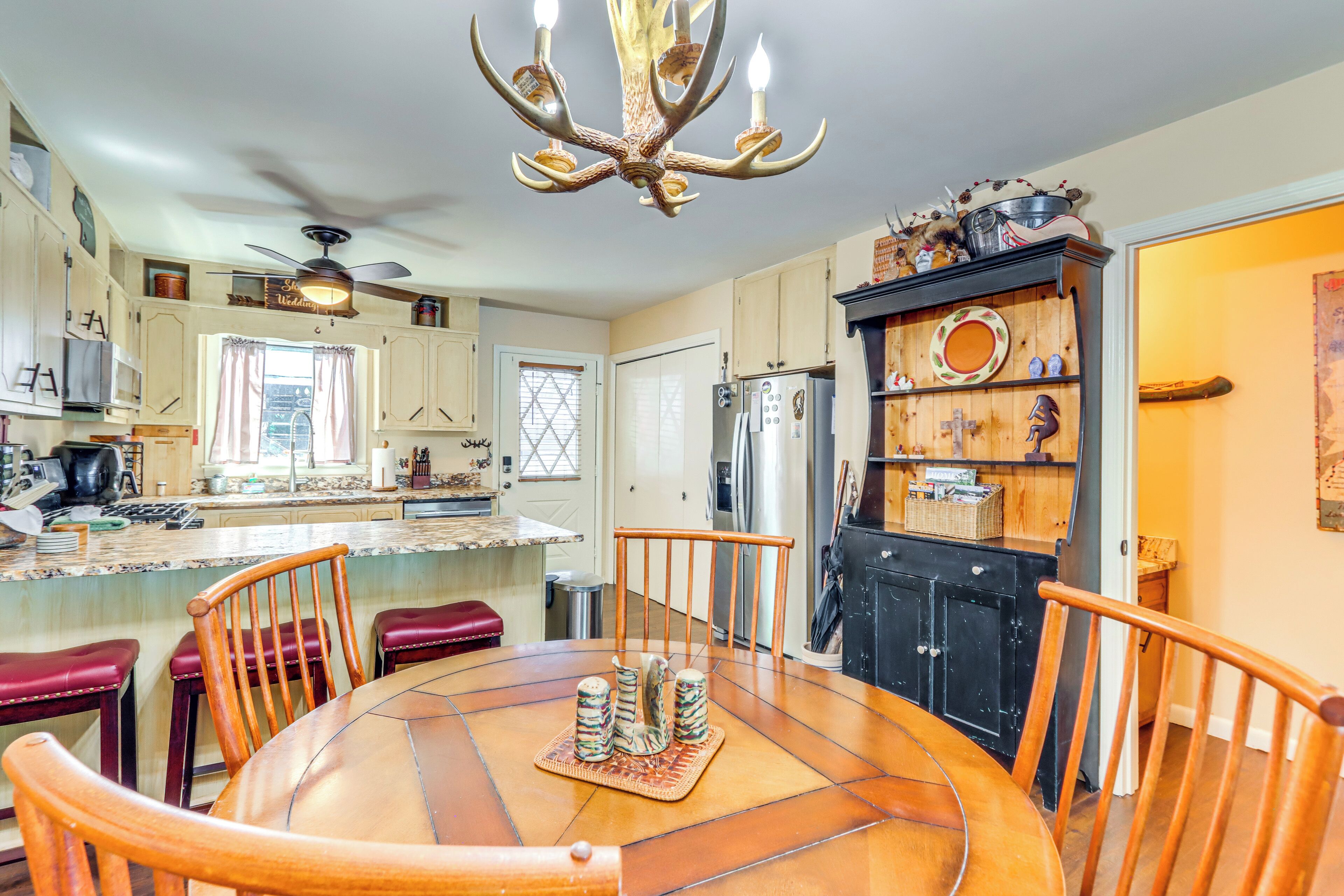 A kitchen with a central island, wooden chairs, a chandelier, and a black cabinet with decorative items.