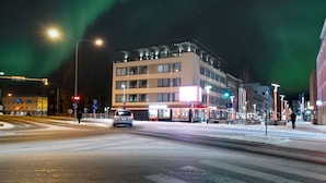 Een meerlaags gebouw met een modern ontwerp, gelegen bij een stadsplein met zichtbare verkeerslichten en straatnaambordjes.