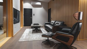 Een moderne woonkamer met een leren bank, een zwarte lederen fauteuil, een bijzettafeltje en een vloerlamp.