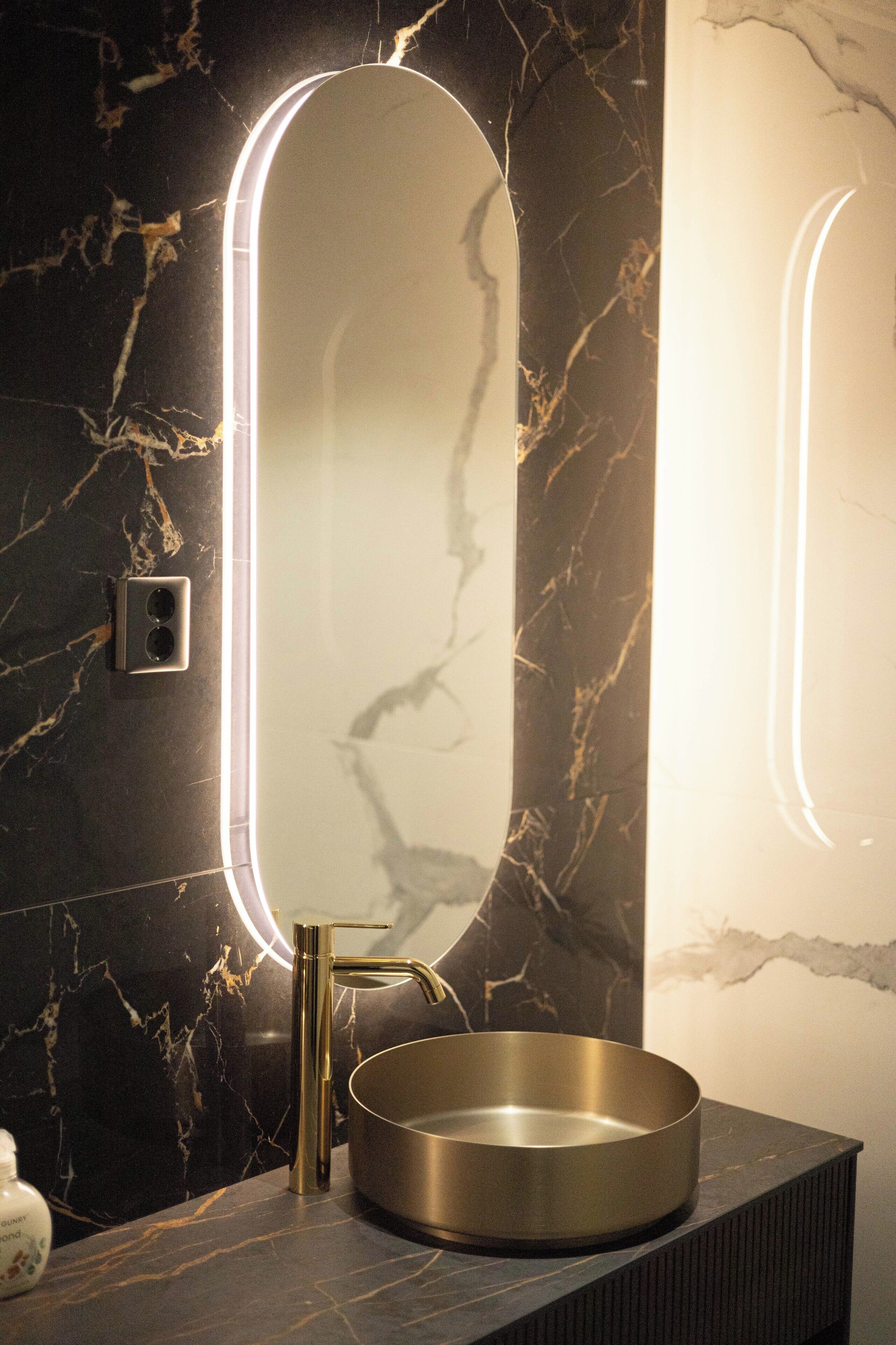 Un baño con lavamanos de mármol, grifo dorado y espejo con iluminación perimetral.