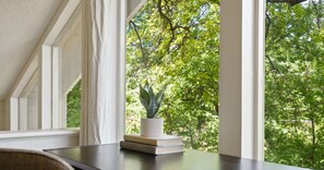 Habitación con ventana que da a un árbol verde y frondoso. Una pequeña planta en maceta está sobre una mesa junto a la ventana.