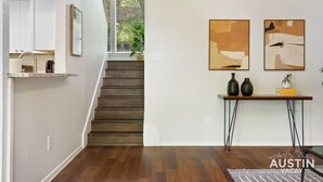 Un interior moderno con una escalera, una zona de cocina y dos cuadros abstractos en la pared.