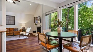 Una sala de estar moderna con comedor, suelo de madera y ventanas amplias con vista a árboles.